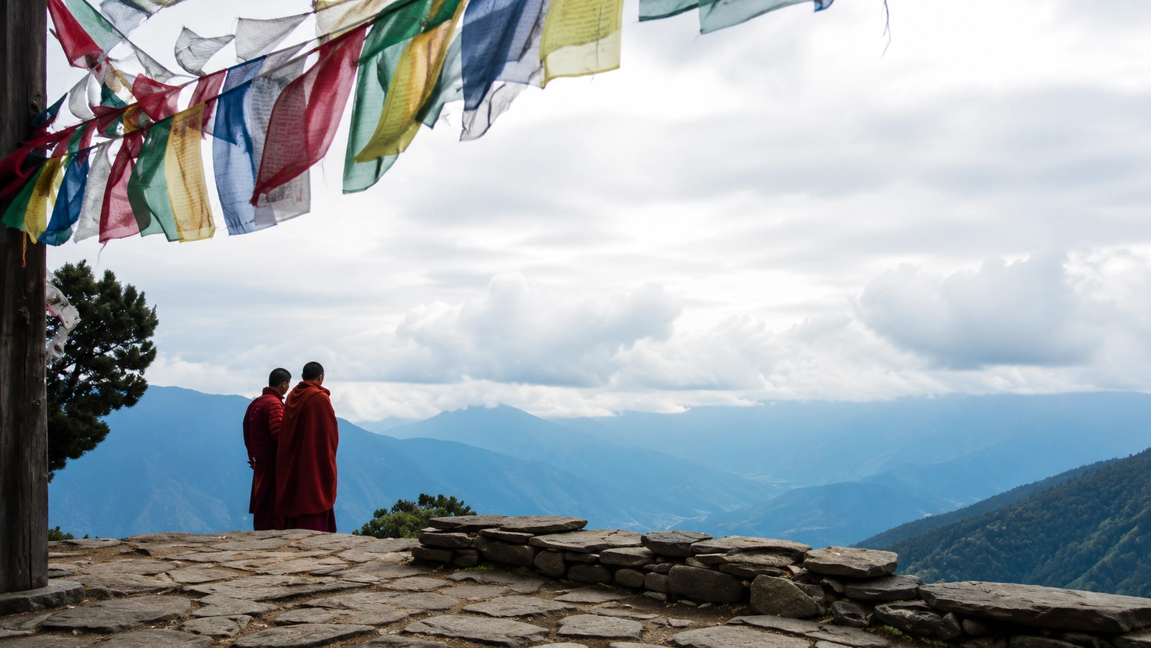 Buddhist monks standing beneath prayer flags overlooking the mountains of Bhutan